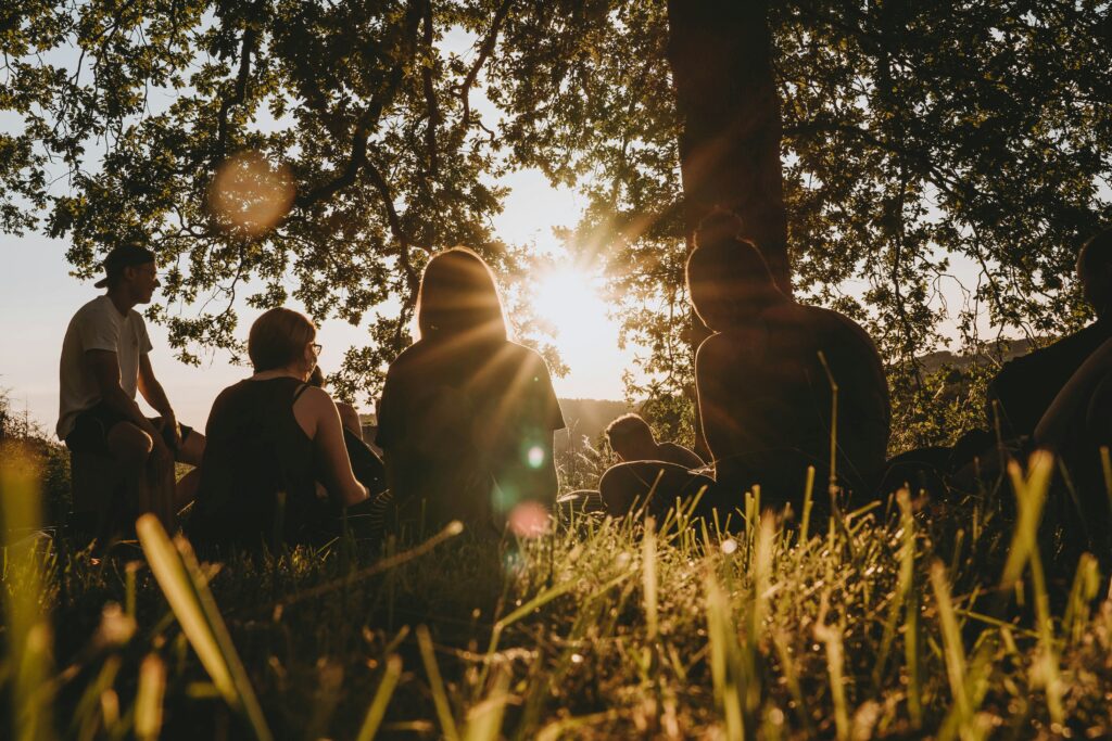 Eine Gruppe junger Menschen sitzt in einem Park, während die Sonne untergeht